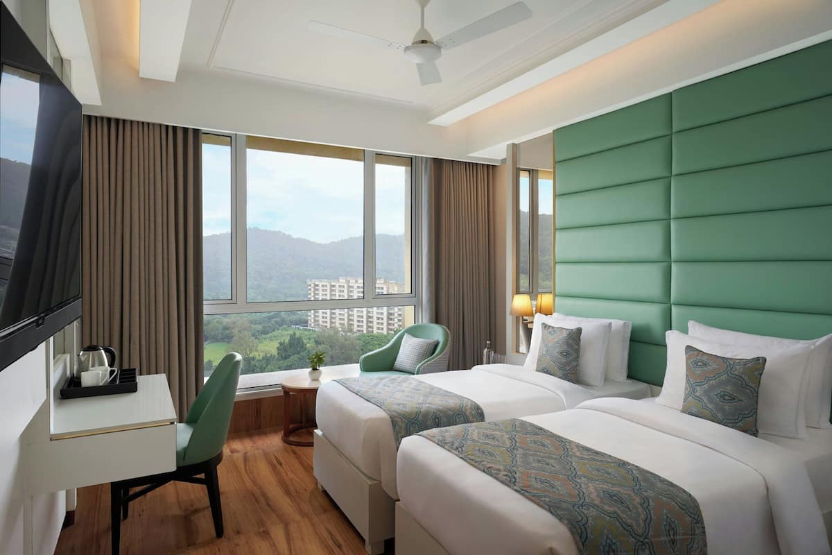 A hotel room with two beds, a desk, a chair, and a TV.