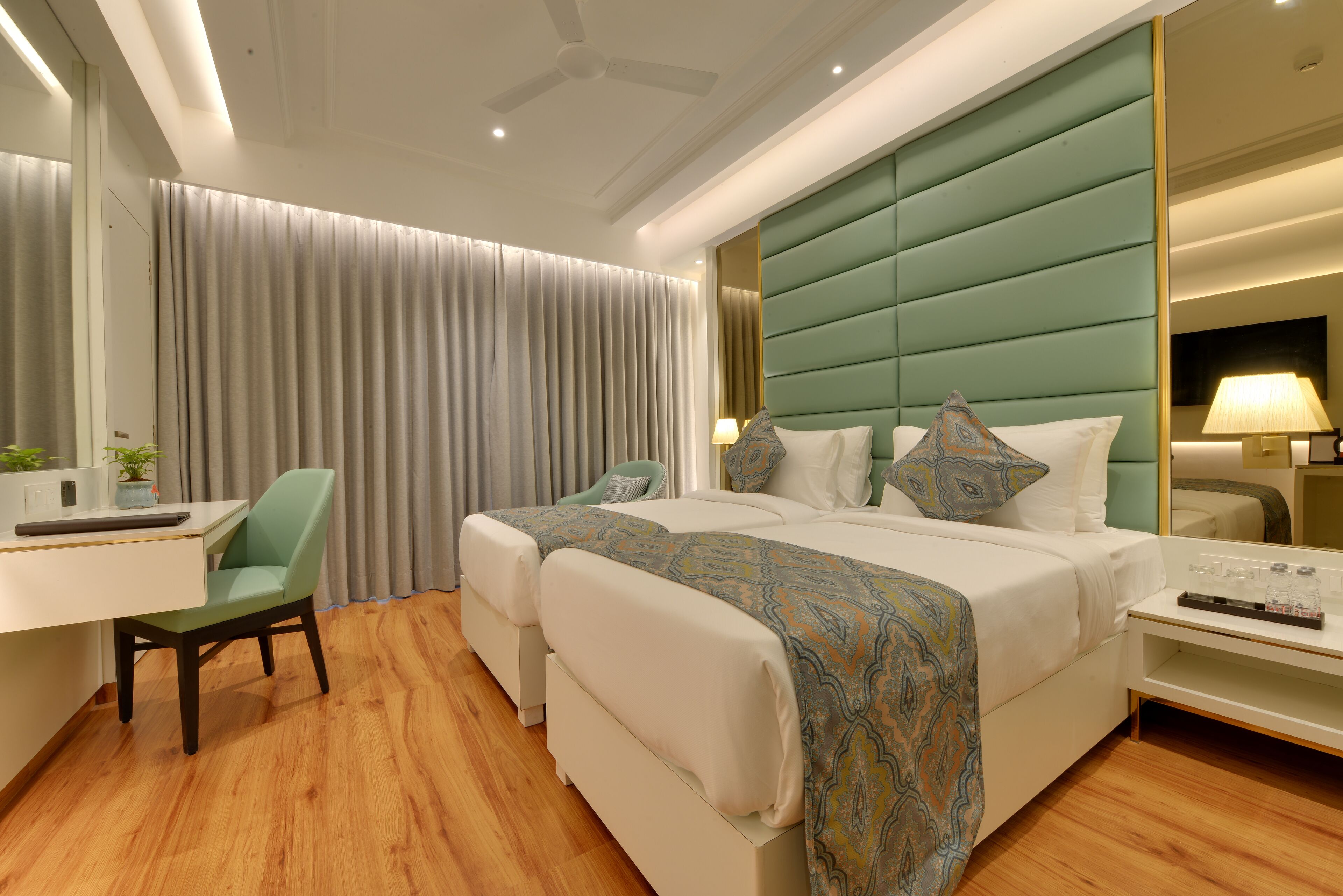 Habitación de hotel con cama, dos mesitas de noche, un escritorio con silla, un espejo y una cortina.