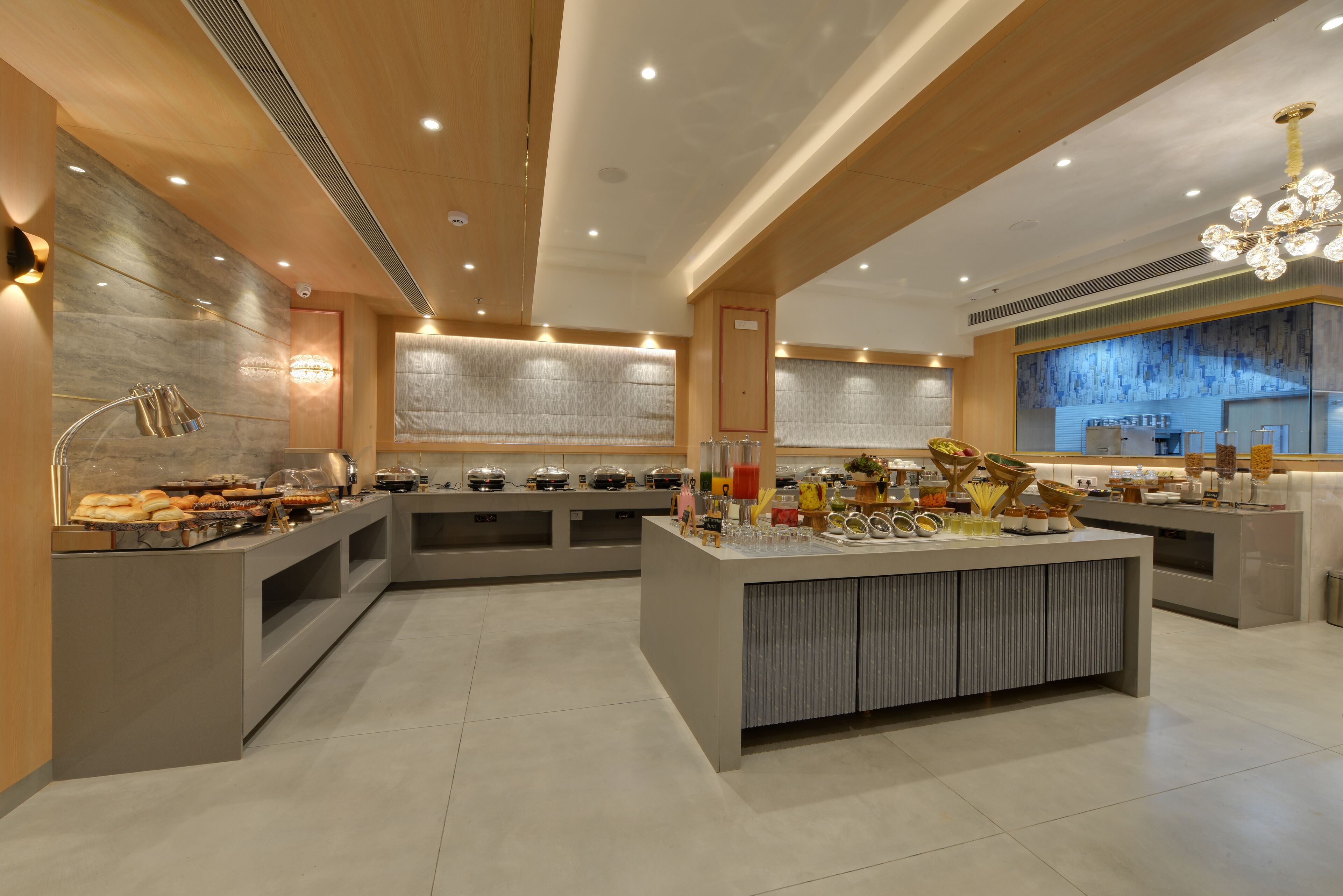 Un hall d’hôtel moderne doté d’un îlot central où se trouve un buffet, des espaces salon et un grand lustre.
