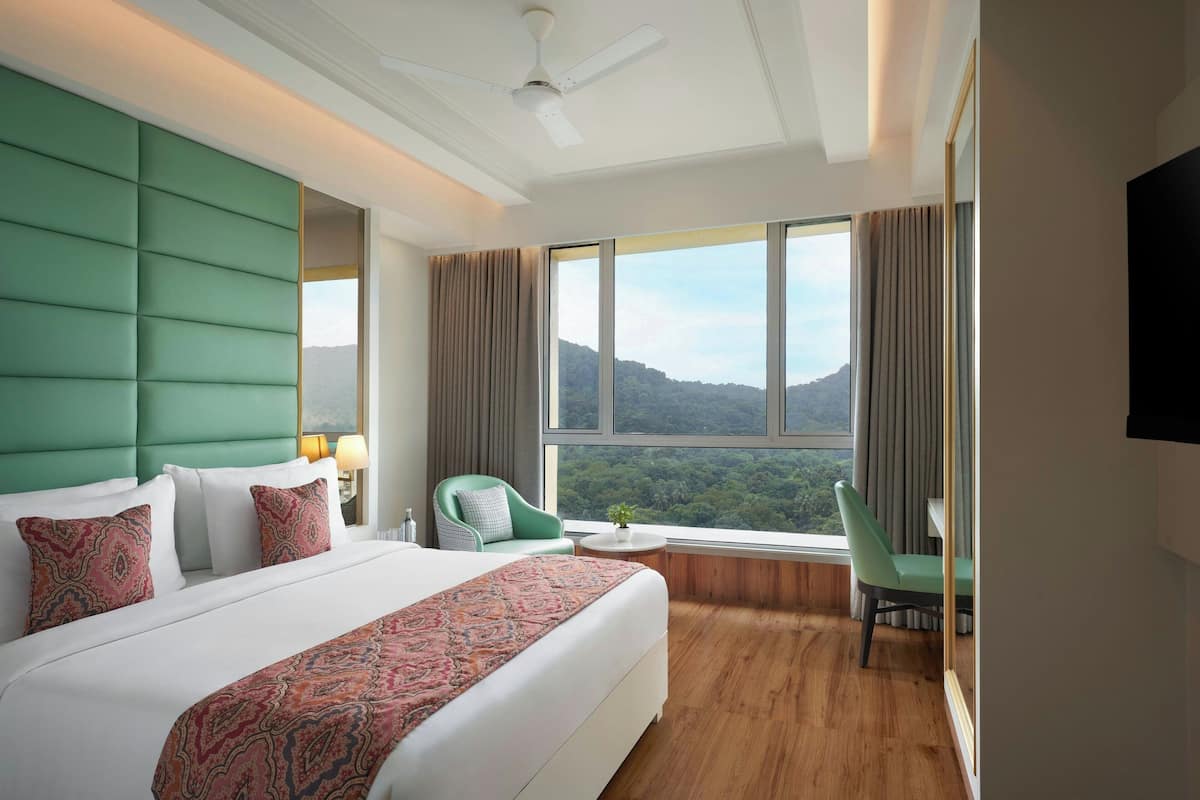 A hotel room with a large bed, a green headboard, a view of the mountains, a desk, and a chair.