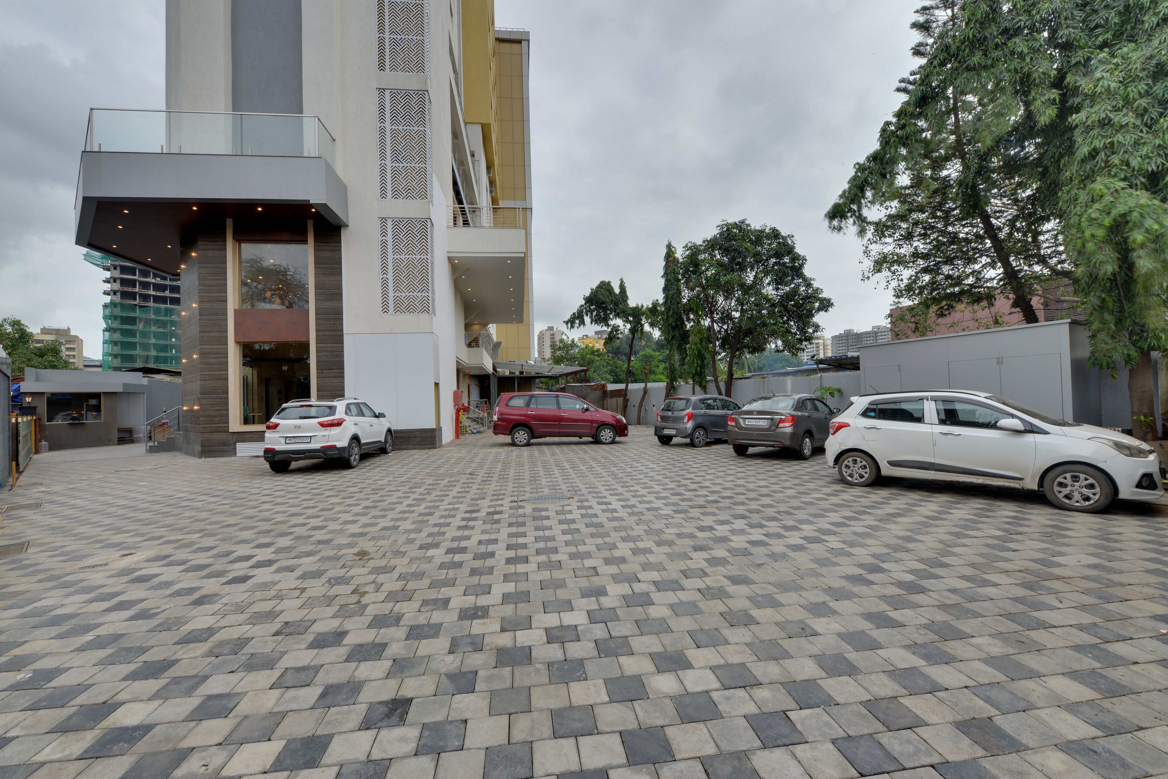 A modern building with a glass balcony, a parking area with several cars, and a checkered pavement.