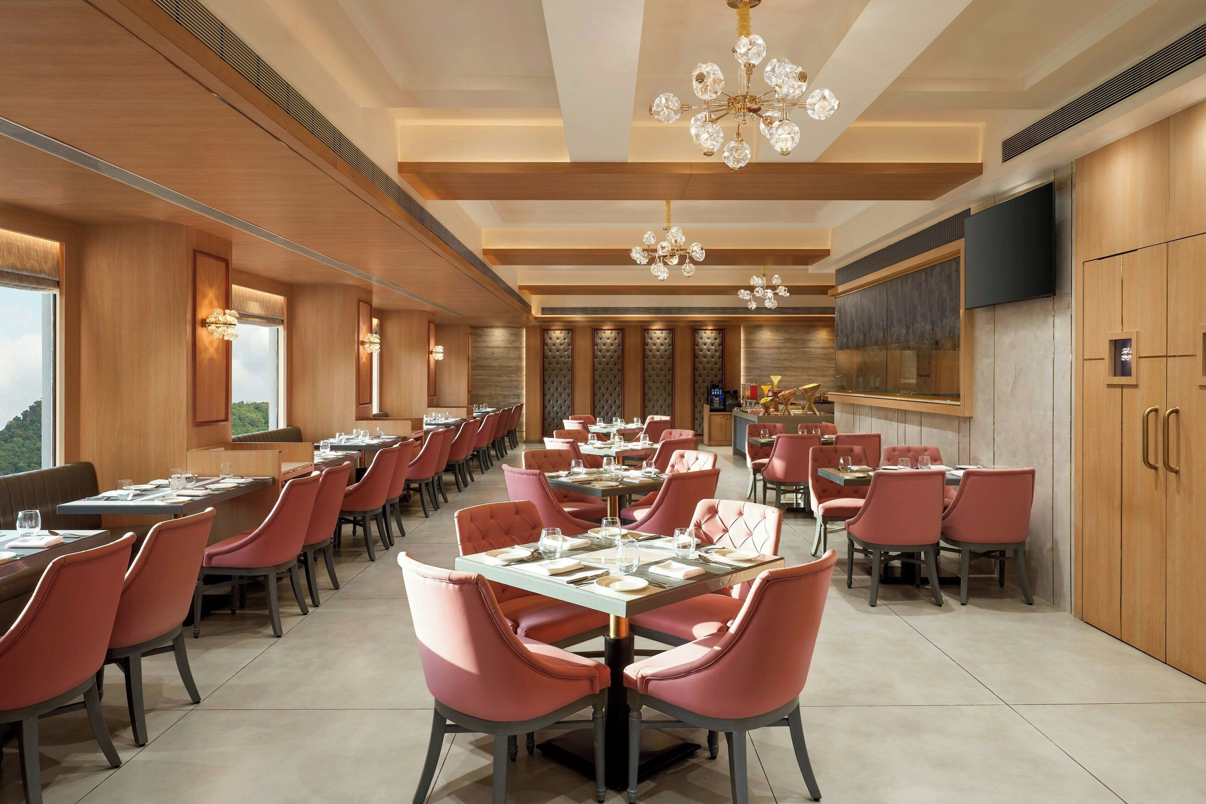 A spacious dining area with multiple tables and chairs, a chandelier, and a large television on the wall.