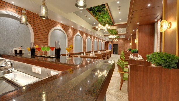 A modern restaurant with a long counter, seating area, and a brick wall. - The Fern Residency Mumbai, Mira Road, Series by Marriott (Mumbai)