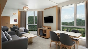 A modern hotel room with a large window, a flat-screen TV, a dining area, and a seating area with sofas and a coffee table. - The Fern Residency Mumbai, Mira Road, Series by Marriott (Mumbai)