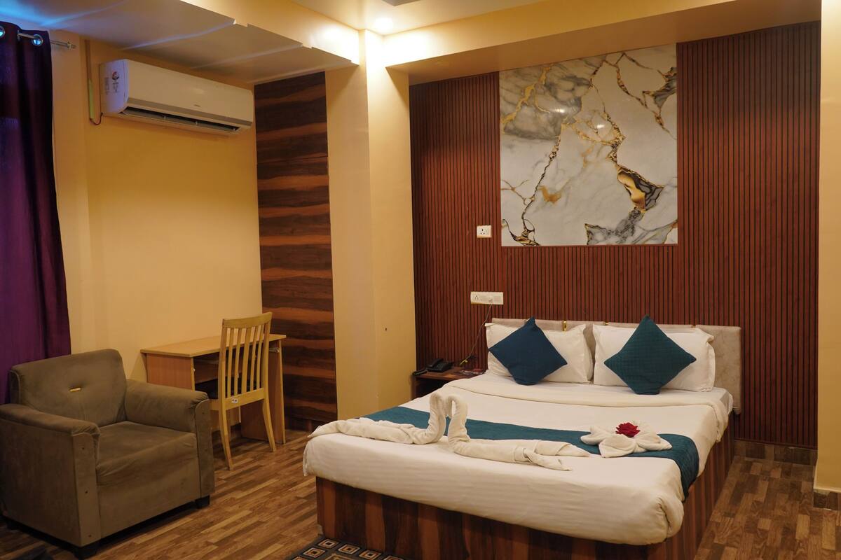 A hotel room with a bed, a desk, a chair, and an air conditioning unit.