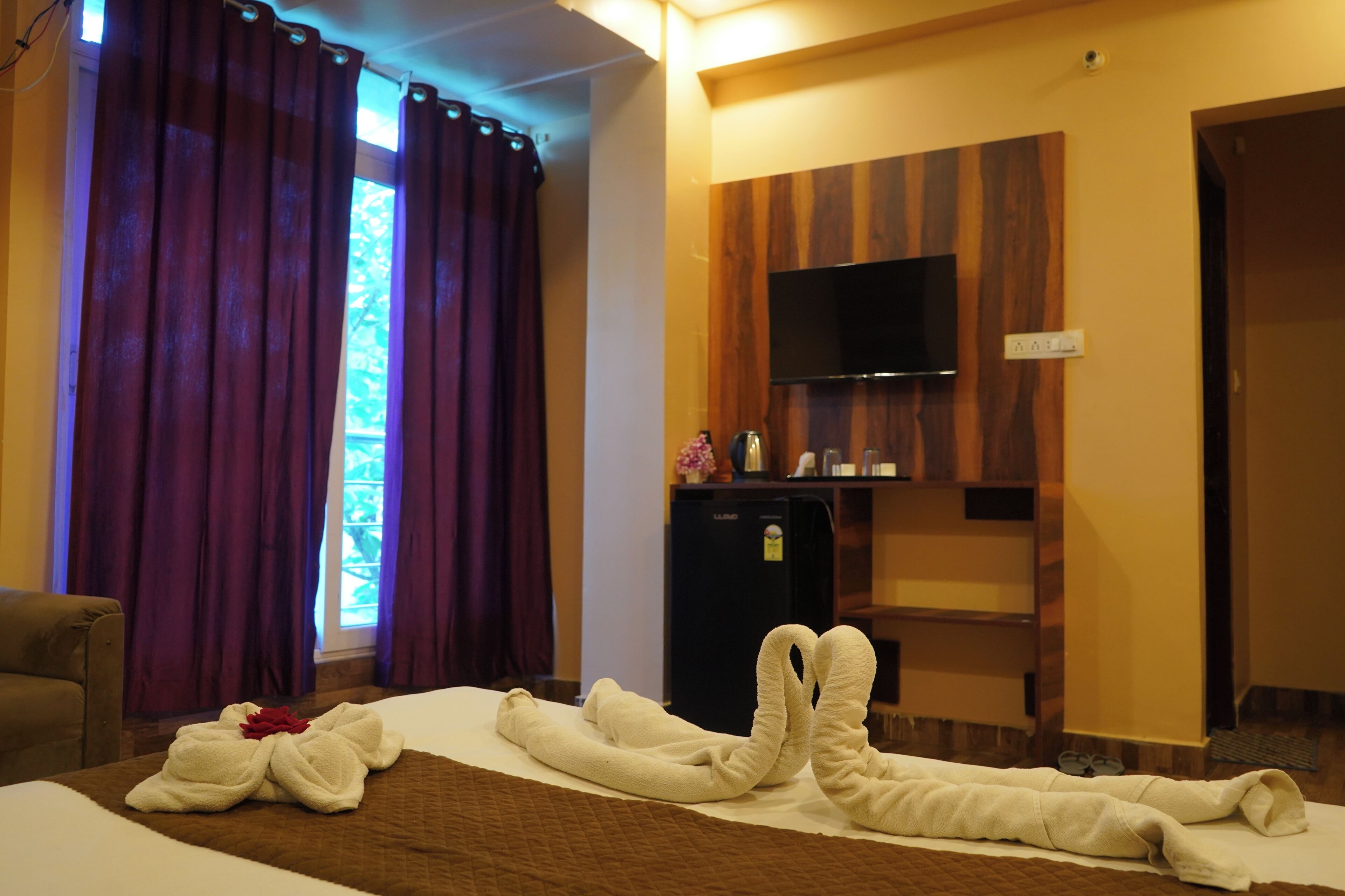 Une chambre d’hôtel avec un lit, un téléviseur fixé au mur, un minibar et une fenêtre avec des rideaux.