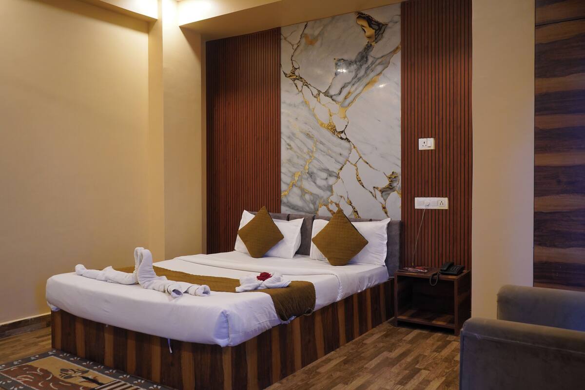 A hotel room with a large bed, wooden paneling, a marble accent wall, and a small bedside table with a phone.