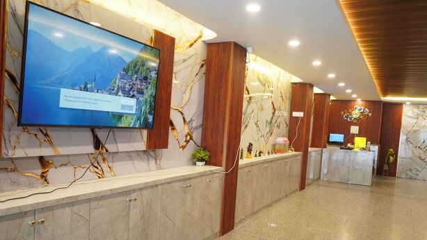 Een hotel receptie met een marmeren balie, een aan de muur bevestigde televisie en een wand van hout.