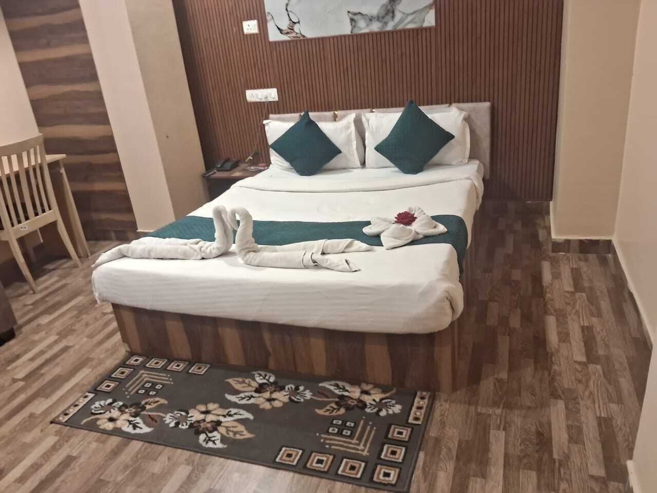A neatly made bed with a white and teal bedspread, two pillows, and a floral rug on a wooden floor.