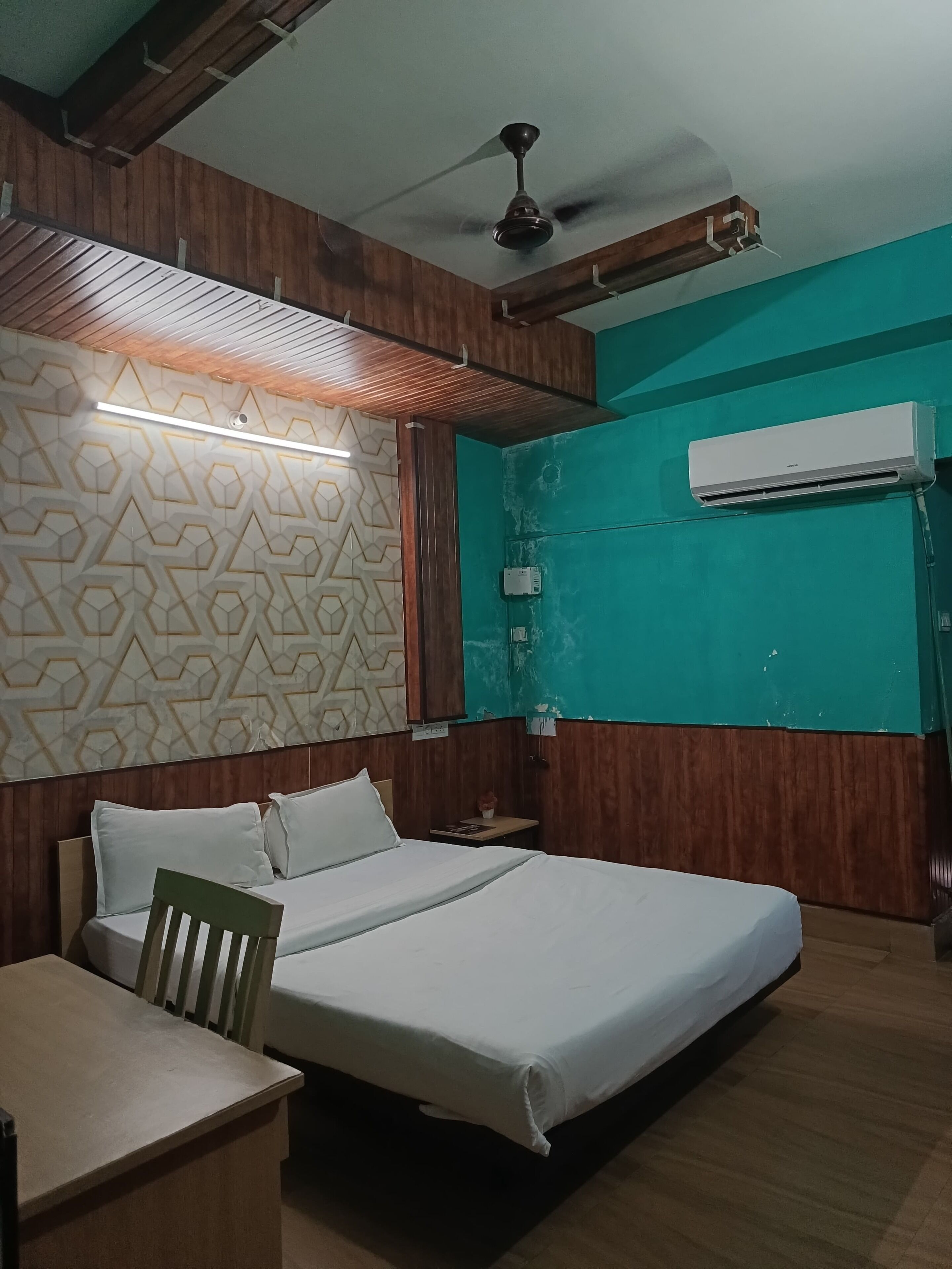 A hotel room with a bed, a desk, a ceiling fan, and an air conditioning unit.