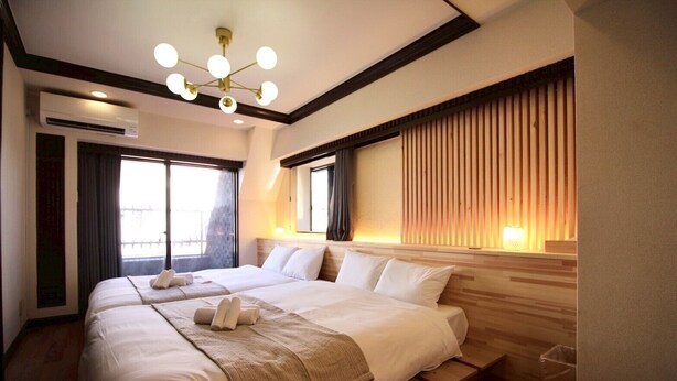 Quarto de hotel com uma cama grande, luminária no teto e janela com cortinas.