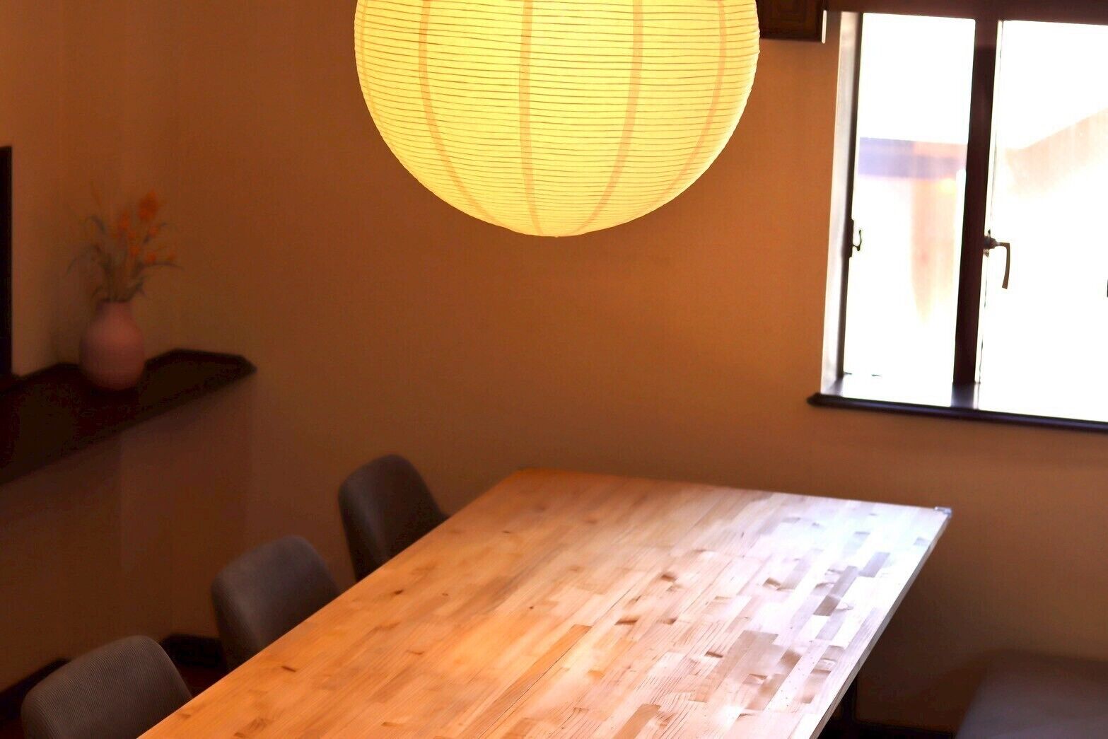 A wooden table with chairs, a hanging light fixture, and a window with a view.