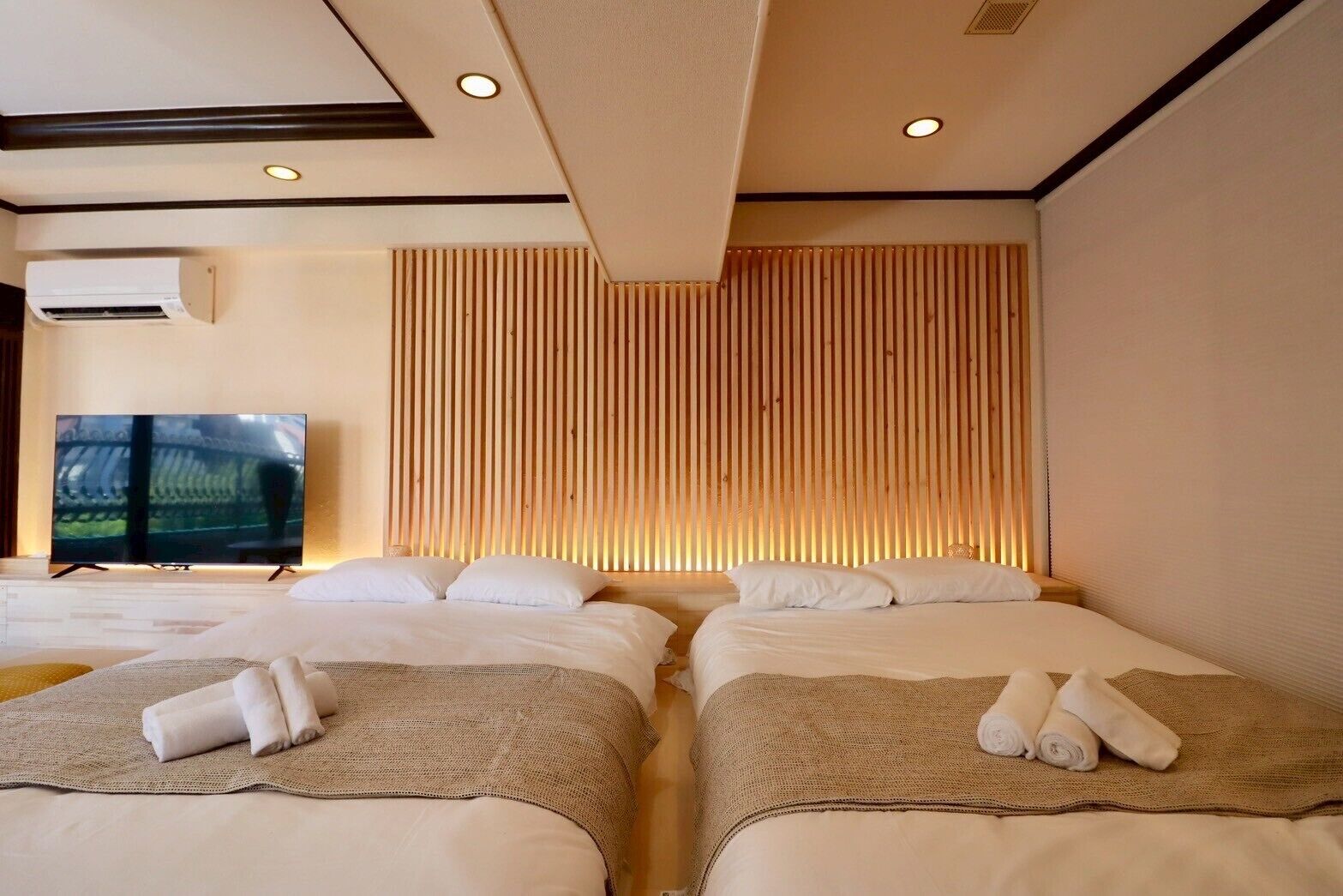 Habitación de hotel con dos camas, un televisor de pantalla plana y cabecera de madera con listones.