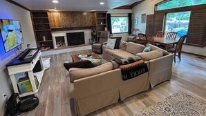 A modern living room with a sectional sofa, a flat-screen TV, a fireplace, and a dining area with a table and chairs. - 6 bedrooms + office + fireplace + firepit + outdoor dining (Arvada)