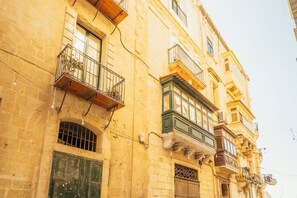 A multi-story building with balconies, a green door, and a window with a barred design. - 🇲🇹 Apartment in the heart of Valletta (IL-BELT VALLETTA)