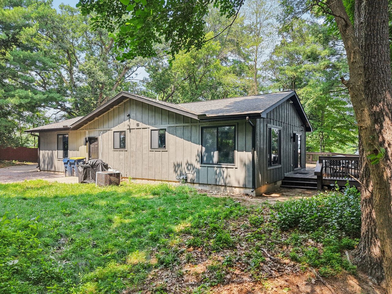 A single-story house with a front porch, a covered patio, and a yard with grass and trees.