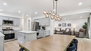 A modern kitchen with stainless steel appliances, a wooden dining table, and a living area with a sofa and armchairs.