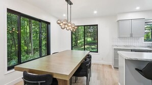 A modern kitchen with large windows, a wooden dining table, and a unique spherical chandelier.