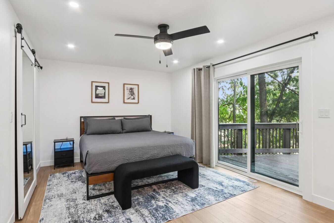 A bedroom with a bed, a bench, a ceiling fan, a window, and a door.
