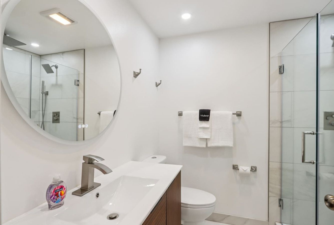 Une salle de bain moderne avec un grand miroir rond, un lavabo, des toilettes et une douche à parois de verre.