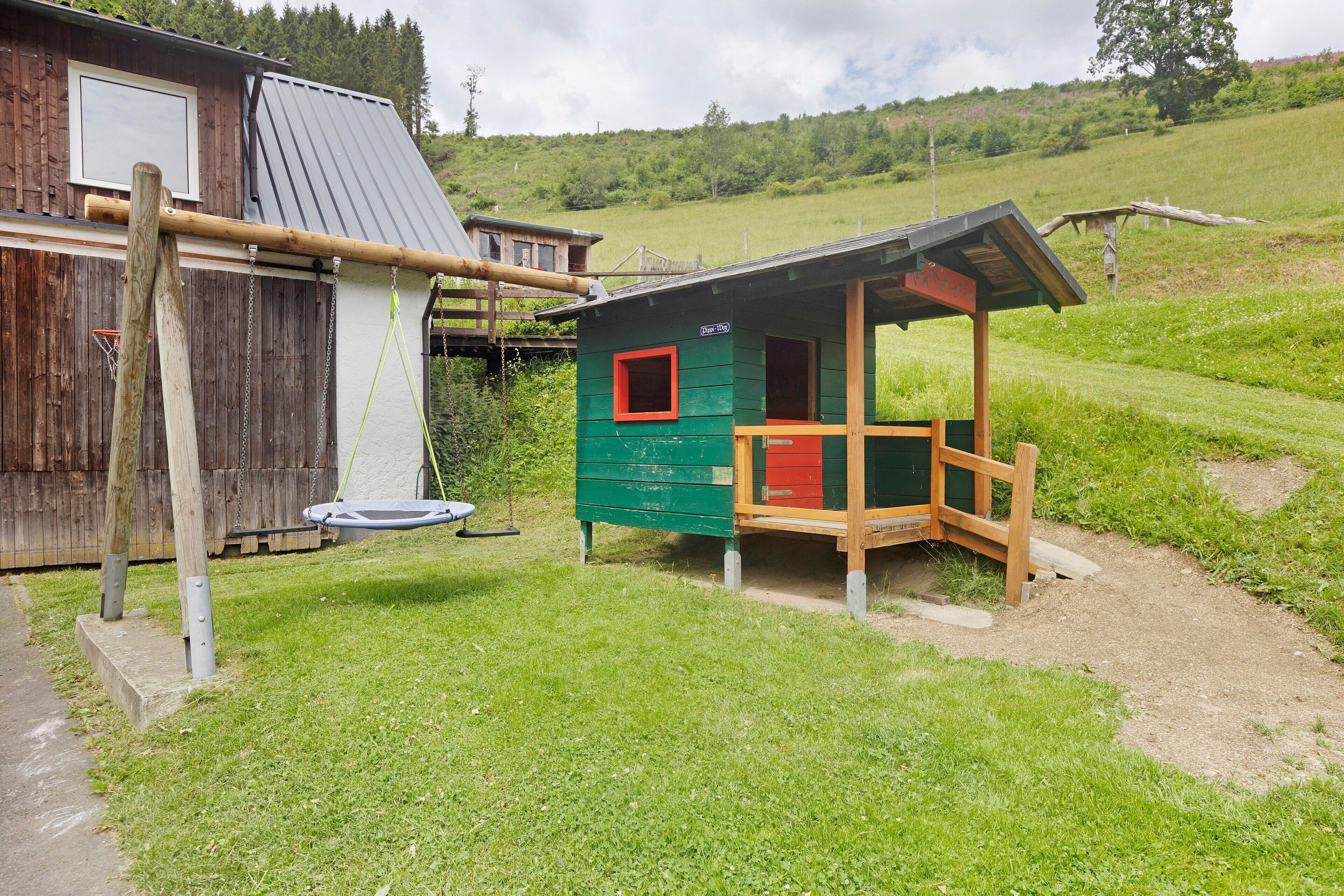 Eine rustikale Holzhütte mit einer kleinen Veranda, einer Schaukel und einem Trampolin auf einer Rasenfläche.