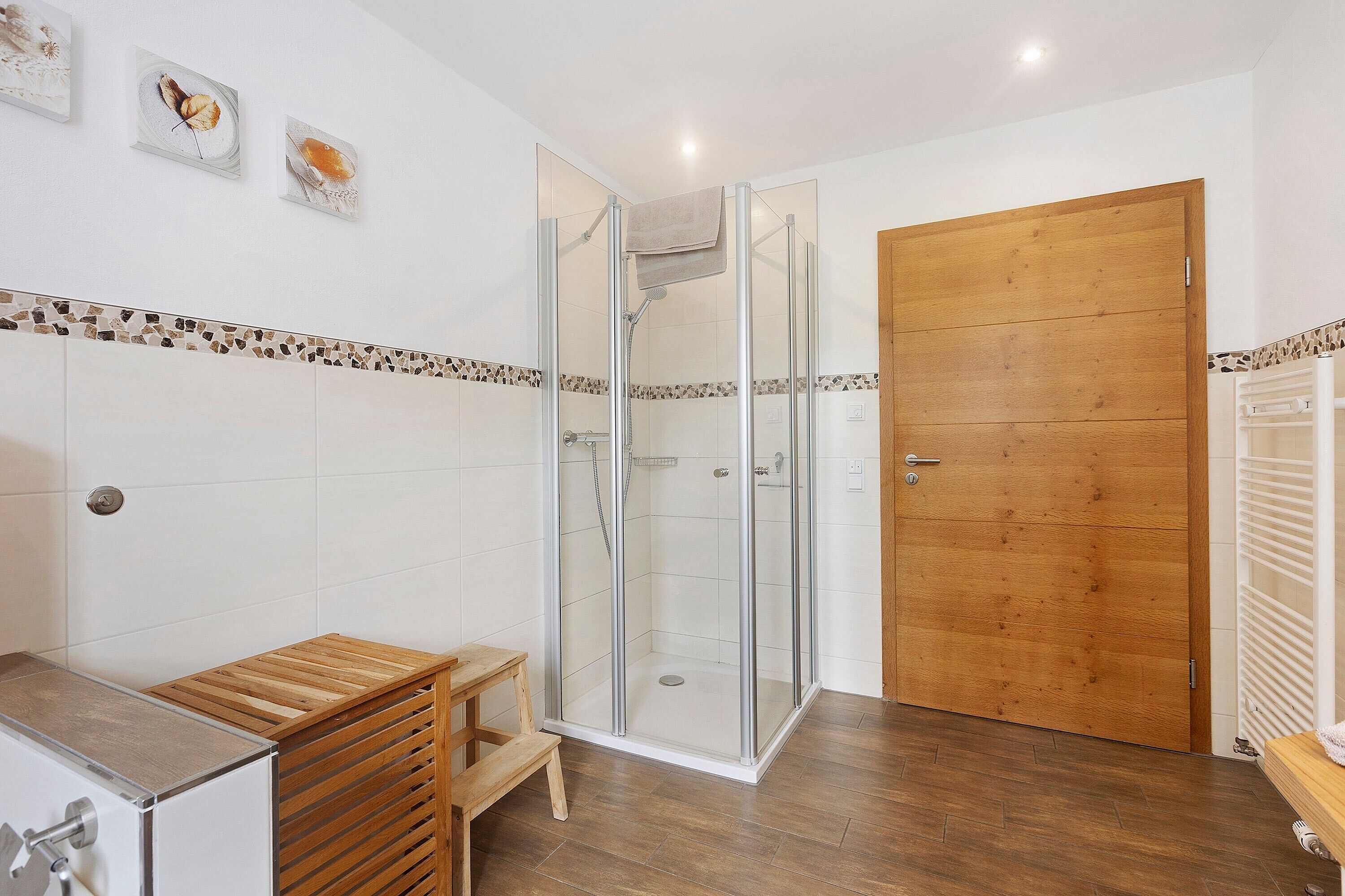 A shower enclosure with a glass door, a wooden door, and a tiled shower area.