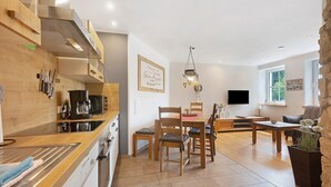 Une cuisine moderne avec des meubles en bois, un coin repas avec une table et des chaises, un mur décoratif en pierre et un téléviseur à écran plat.