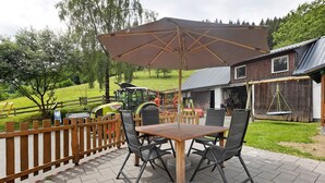 Une terrasse extérieure avec une table et des chaises en bois, un grand parasol et une clôture en bois.