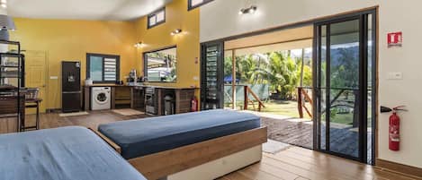 Une chambre compacte comprenant deux lits, une kitchenette, un lave-linge et une porte-fenêtre coulissante donnant sur un balcon.
