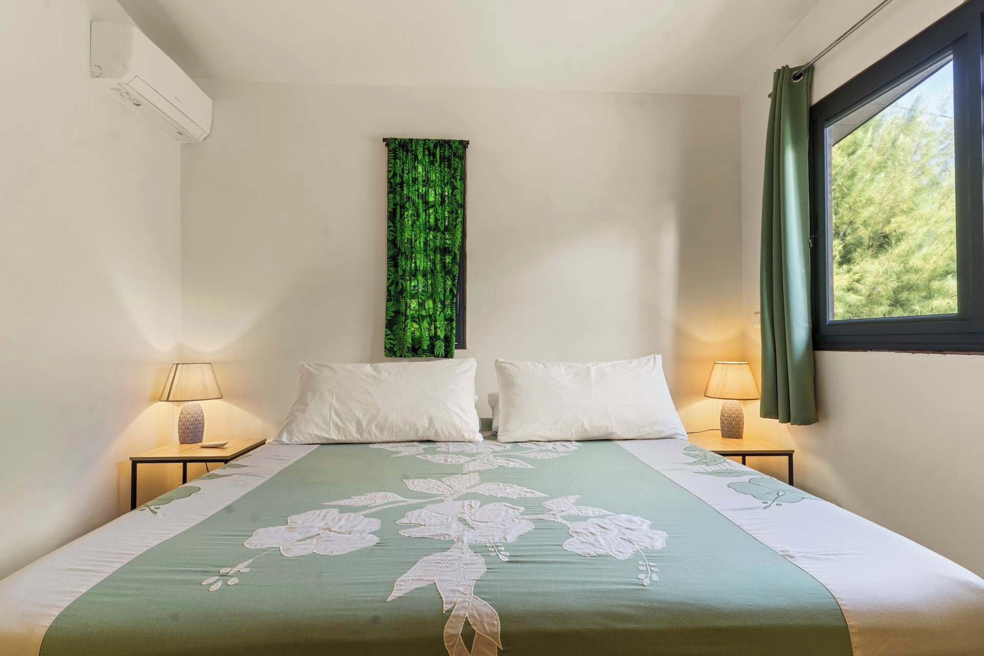 Une chambre à coucher avec un lit, deux lampes de chevet, une fenêtre avec des rideaux et un climatiseur fixé au mur.