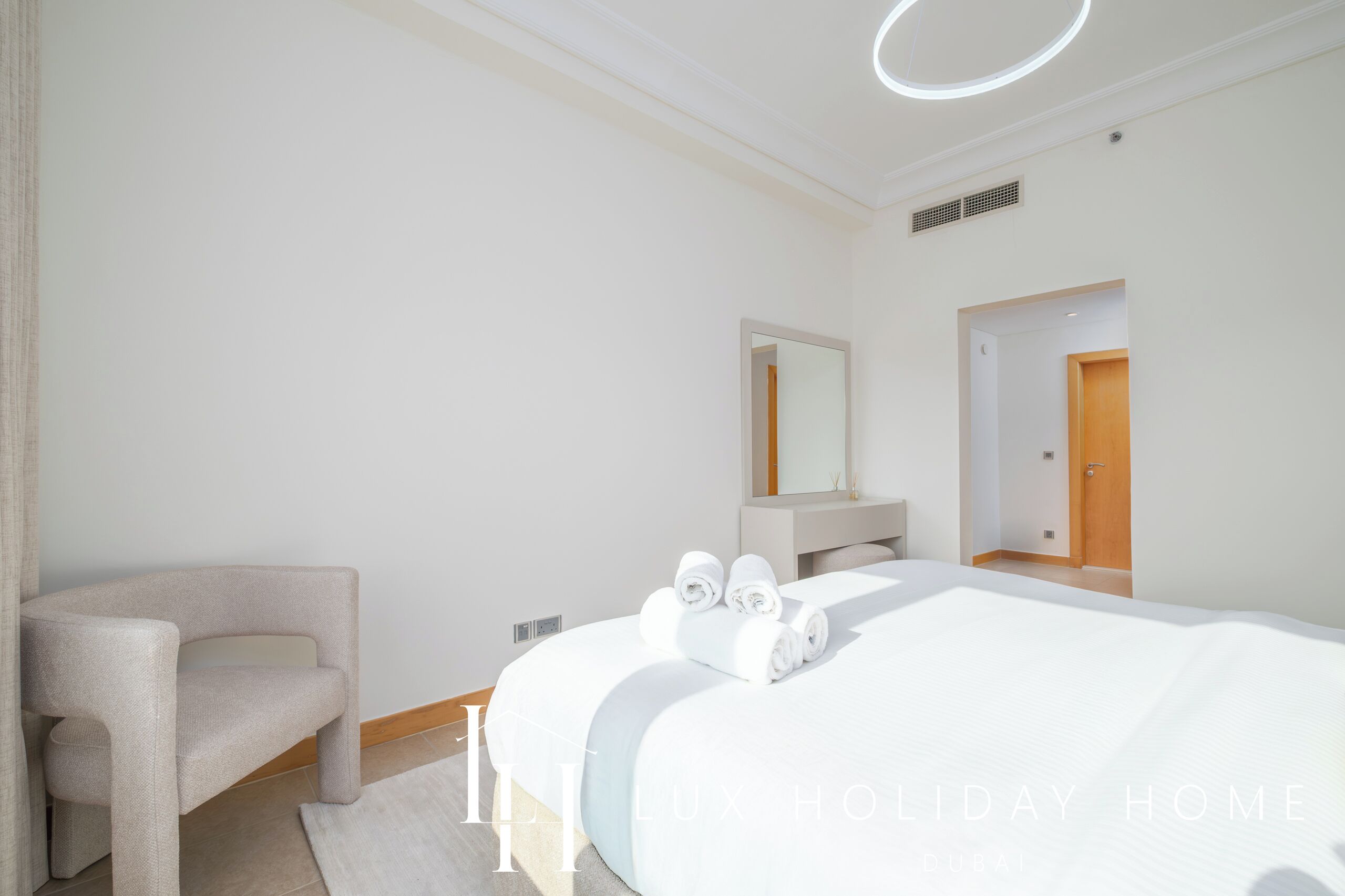 Une chambre d’hôtel moderne avec un grand lit, une chaise, une coiffeuse avec un miroir et une porte.