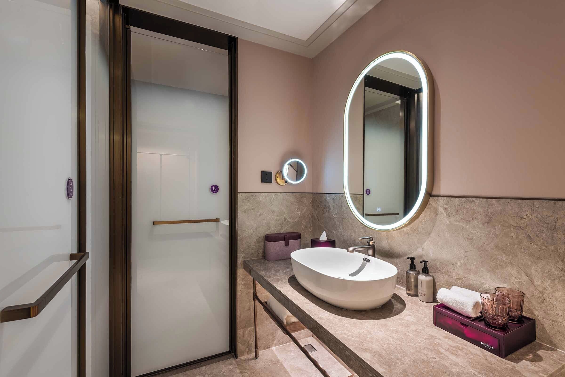 Um banheiro moderno com uma grande pia oval, um espelho redondo com iluminação embutida, um porta-toalhas e um lavatório com produtos de higiene pessoal.