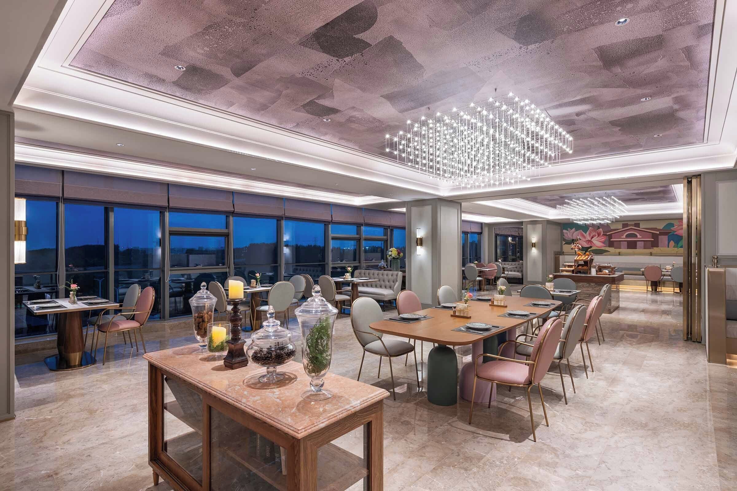 Un vaste espace dédié à la salle à manger, avec de nombreuses tables et chaises, de grandes fenêtres et un lustre moderne.