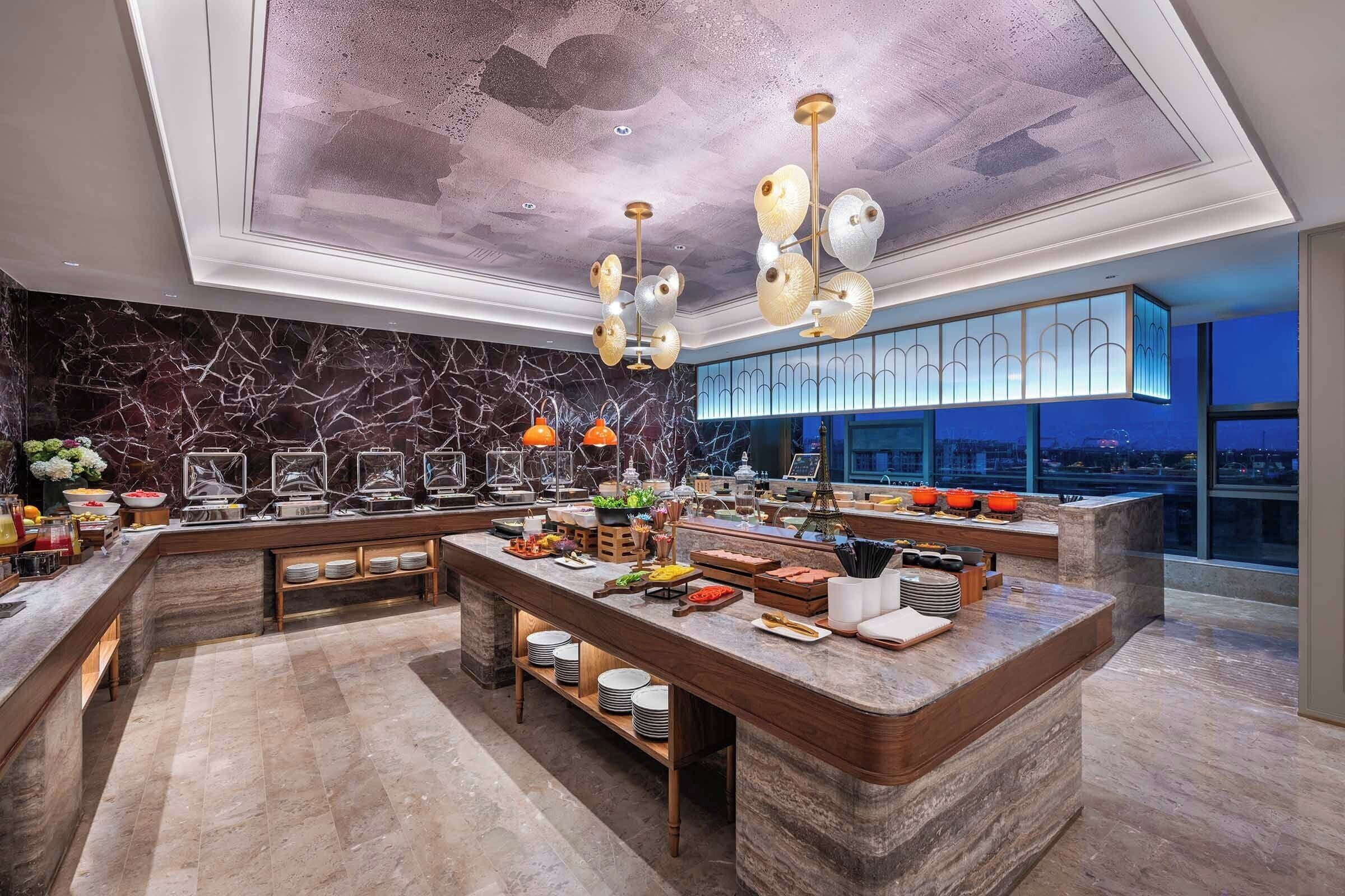 A modern hotel lobby with a marble reception desk, a high ceiling with a unique design, and a view of the city at night.
