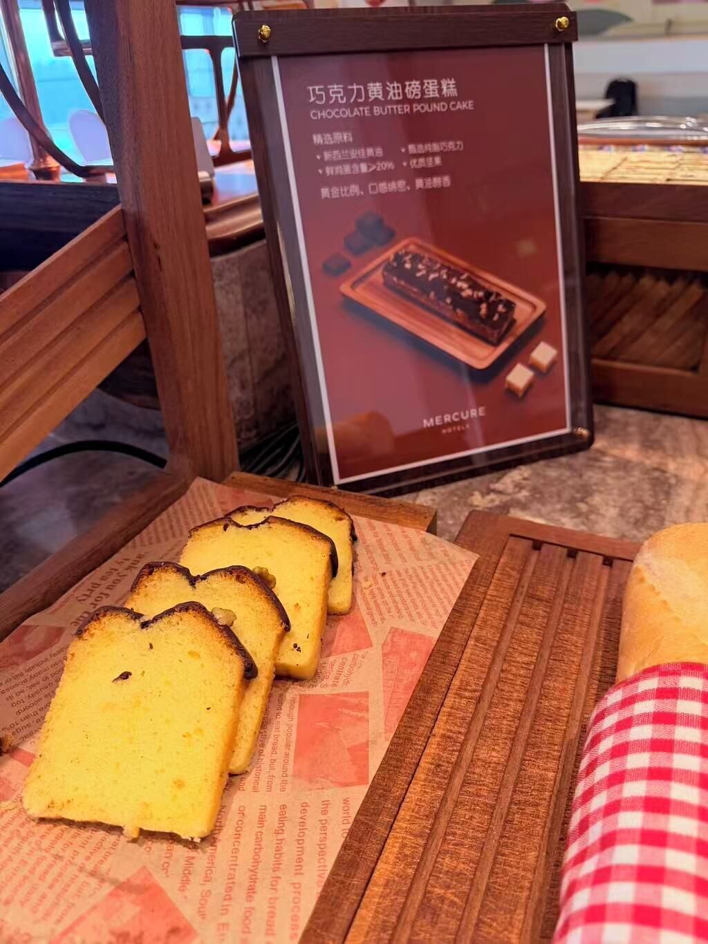 A menu board with a chocolate butter pound cake and slices of bread on a wooden table.