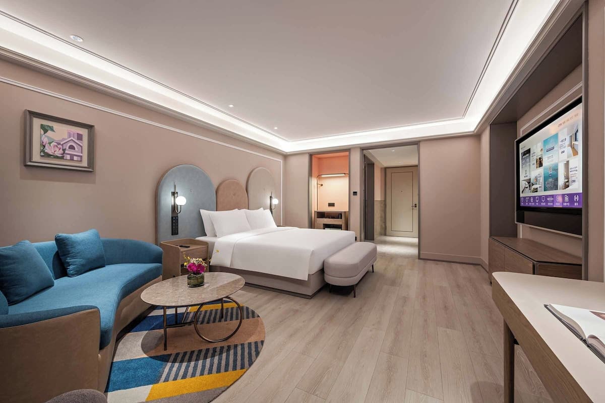 A modern hotel room with a bed, sofa, TV, and a small table.