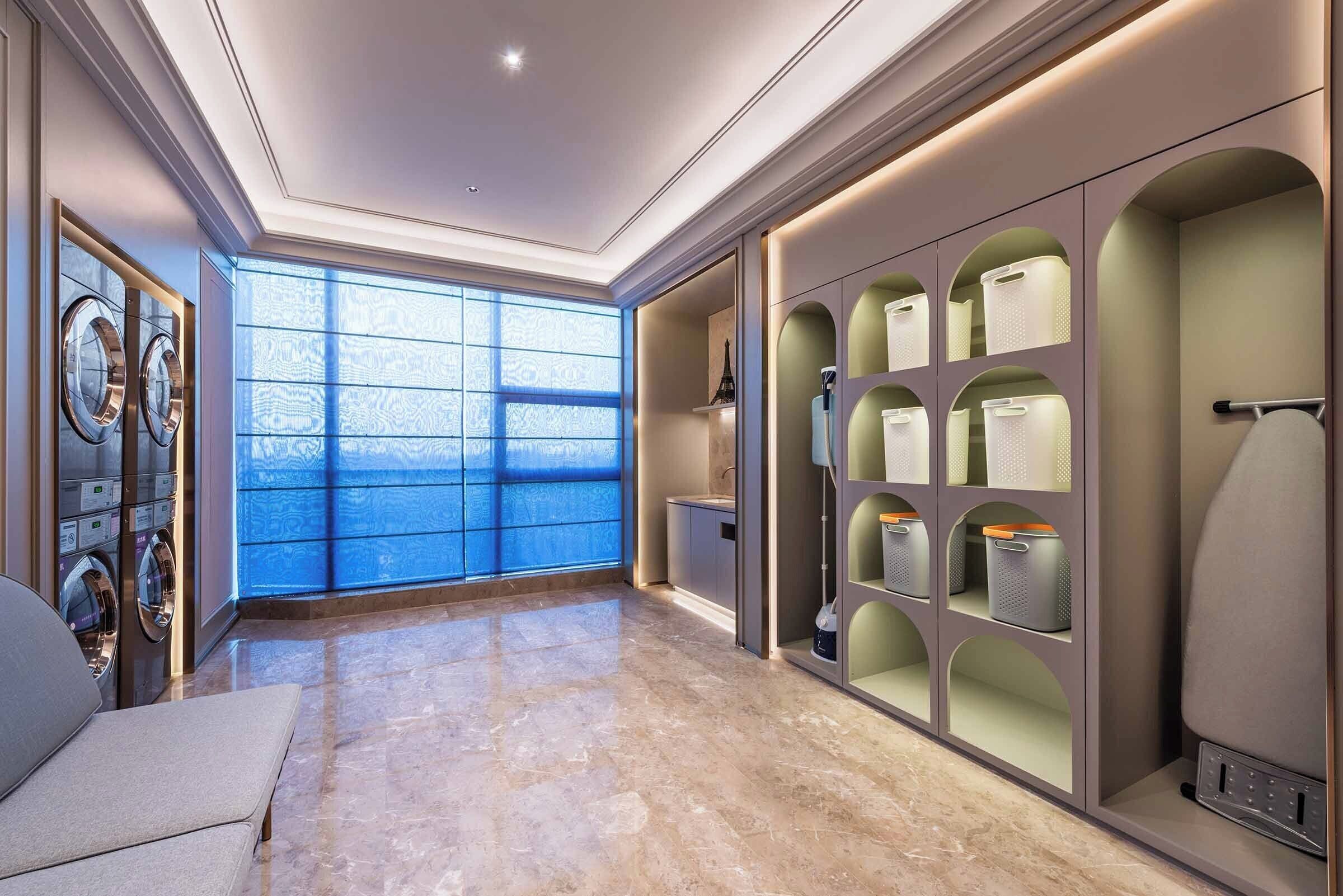 Una habitación de hotel moderna con un ventanal grande, lavadora y secadora integradas, y un almacenaje con varios compartimentos.