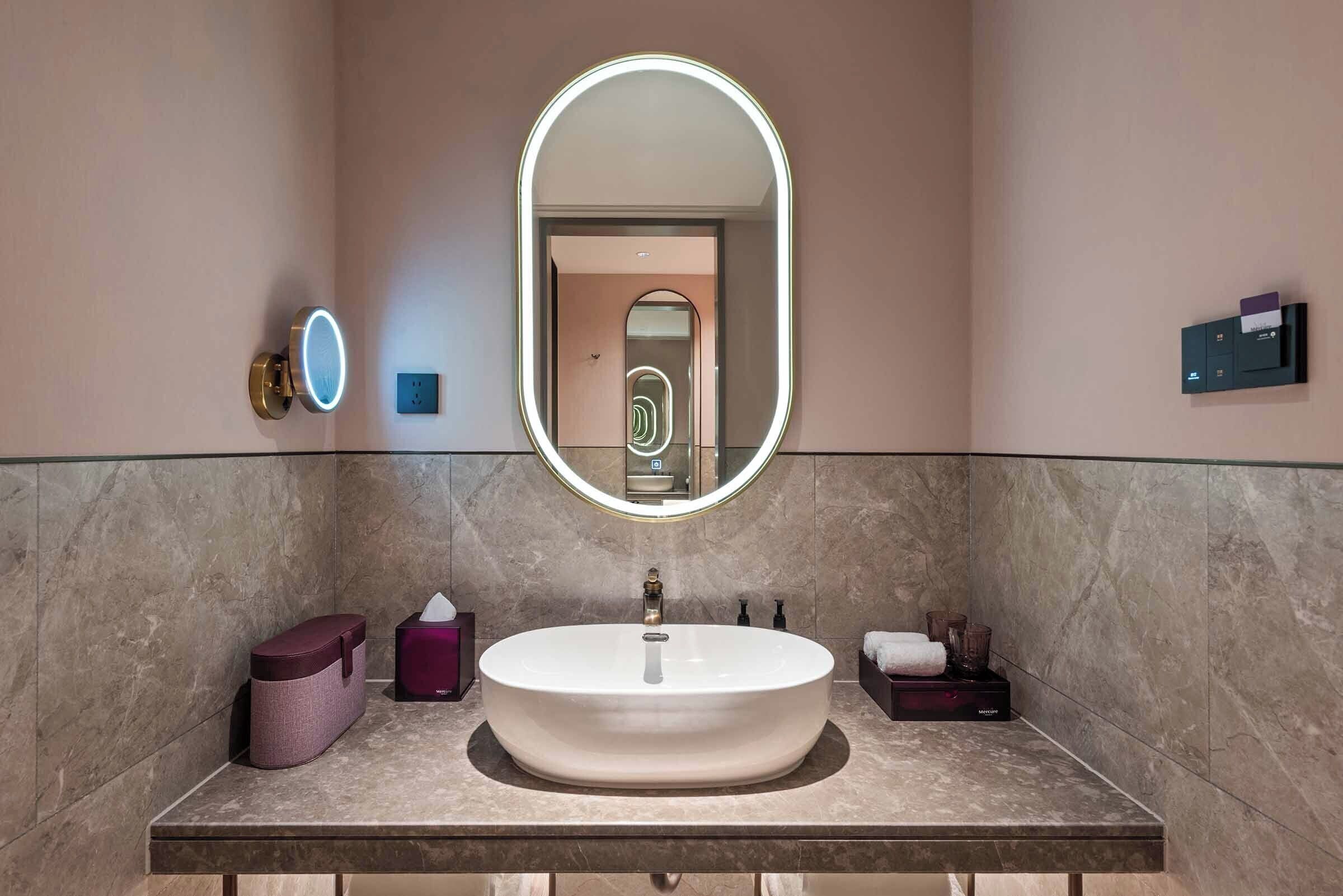 Un bagno con un ampio lavandino ovale, uno specchio illuminato, un asciugamano e articoli da toilette.