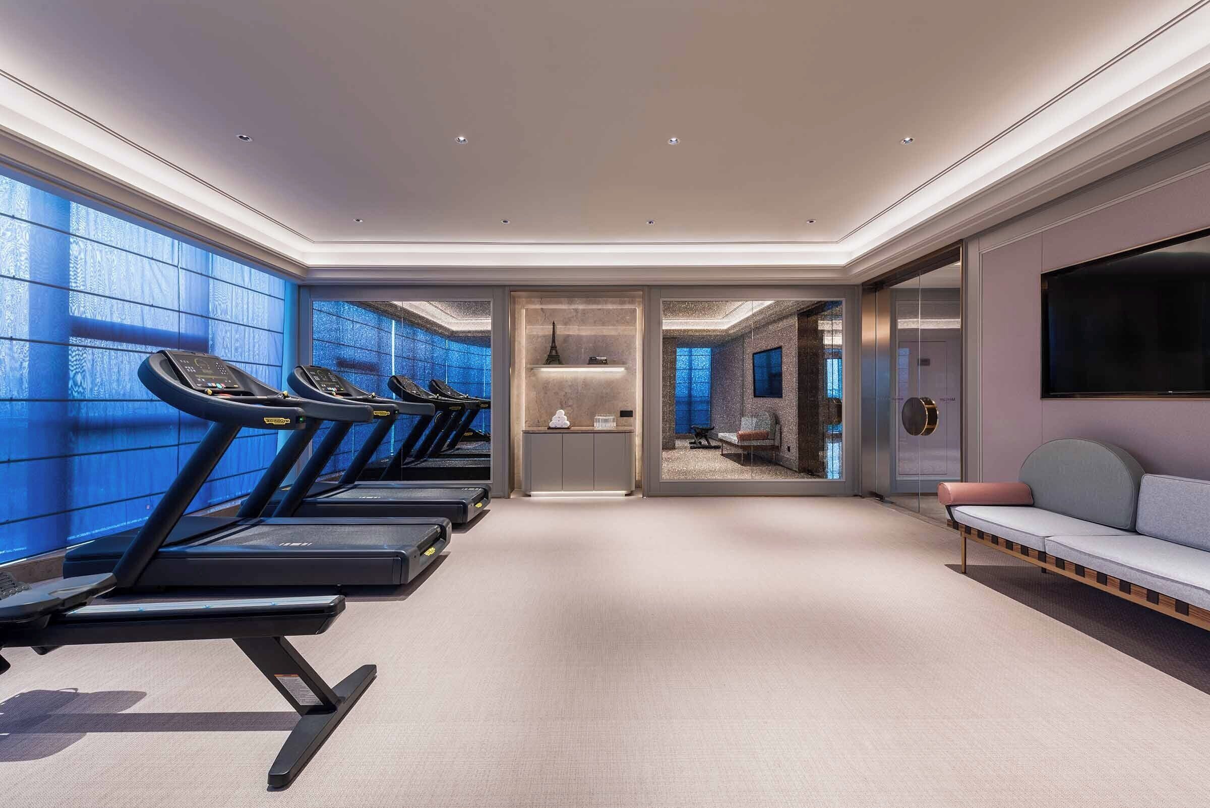Una habitación de hotel moderna con un área de fitness, un sofá y un televisor.