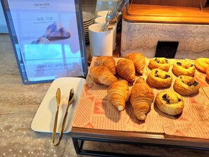 A breakfast buffet with croissants and other pastries, a digital menu board, and a plate with cutlery. - Mercure Nantong Suxitong Riverside (Nantong)