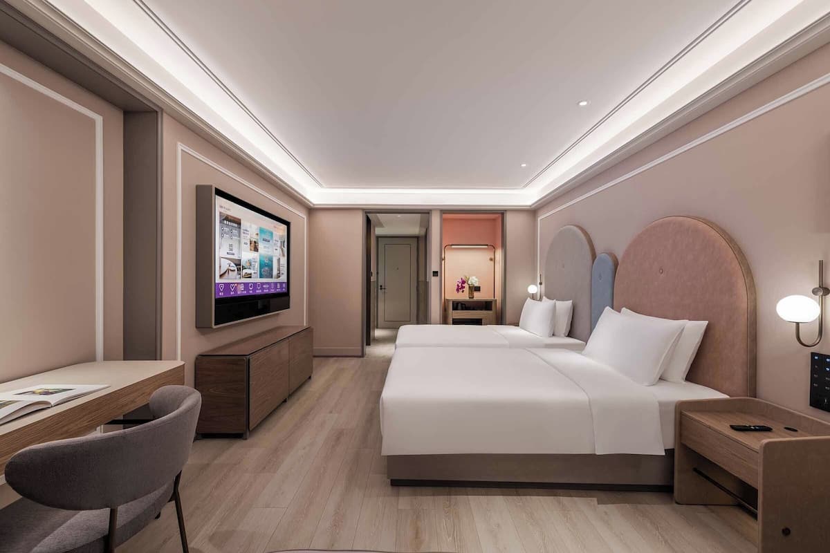 A hotel room with a bed, a desk, a chair, a TV, and a nightstand.