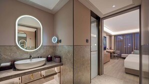 Un baño moderno con un espejo grande, tocador y una zona separada con cama y escritorio.