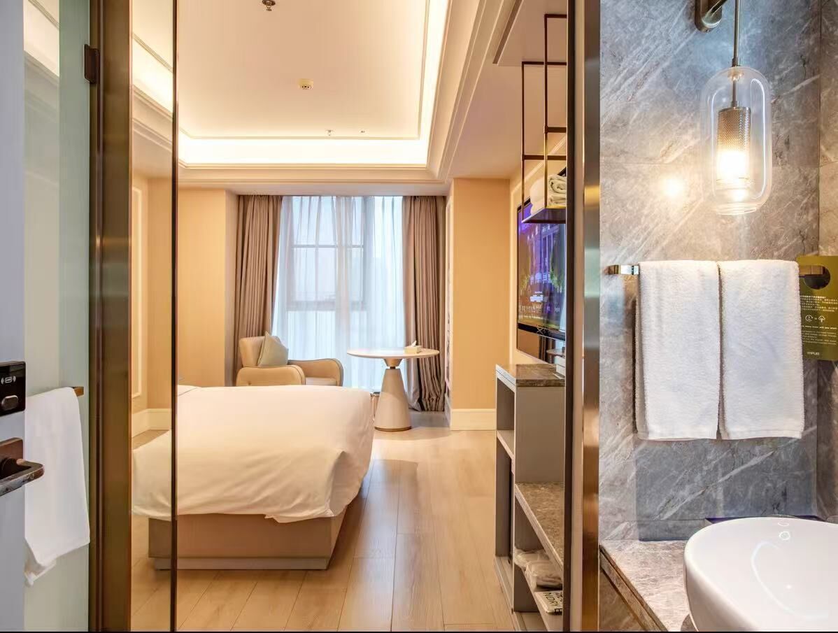 A hotel room with a bed, a seating area with a table, a bathroom with a marble wall and a sink.