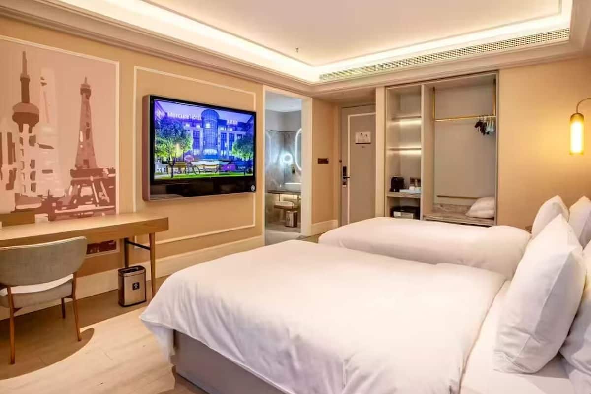 A hotel room with a bed, a desk, a chair, a TV, and a wardrobe.
