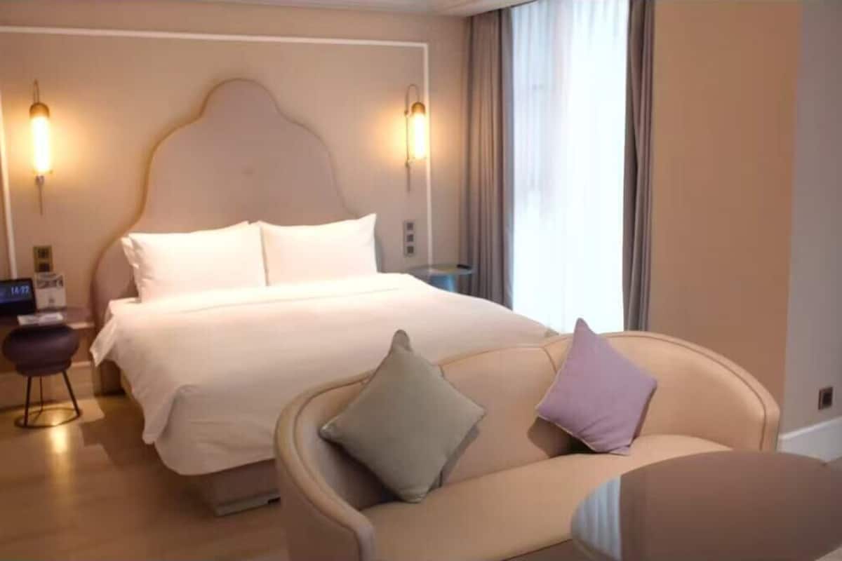 A hotel room with a bed, a sofa, a nightstand, and a lamp.