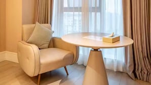 Una habitación moderna con un sillón de cuero color beige, una mesa redonda y cortinas de encaje.