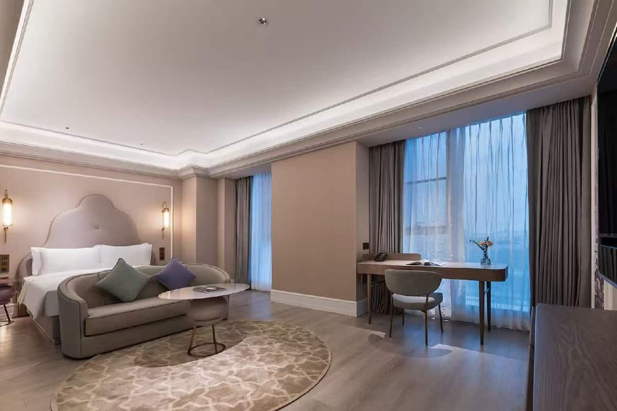 A modern hotel room with a bed, a sofa, a desk, and a dining area.