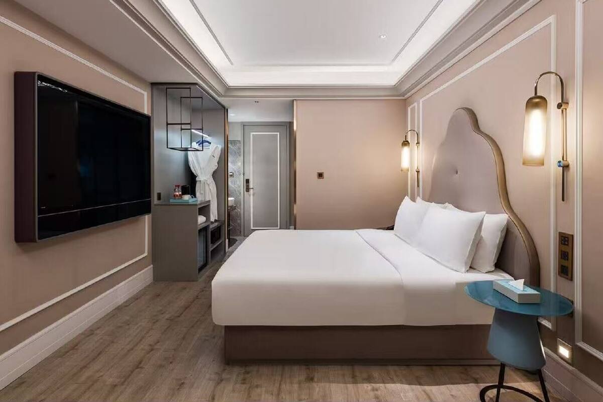 A modern hotel room with a large bed, a flat-screen TV, a vanity with a mirror, and a small table.