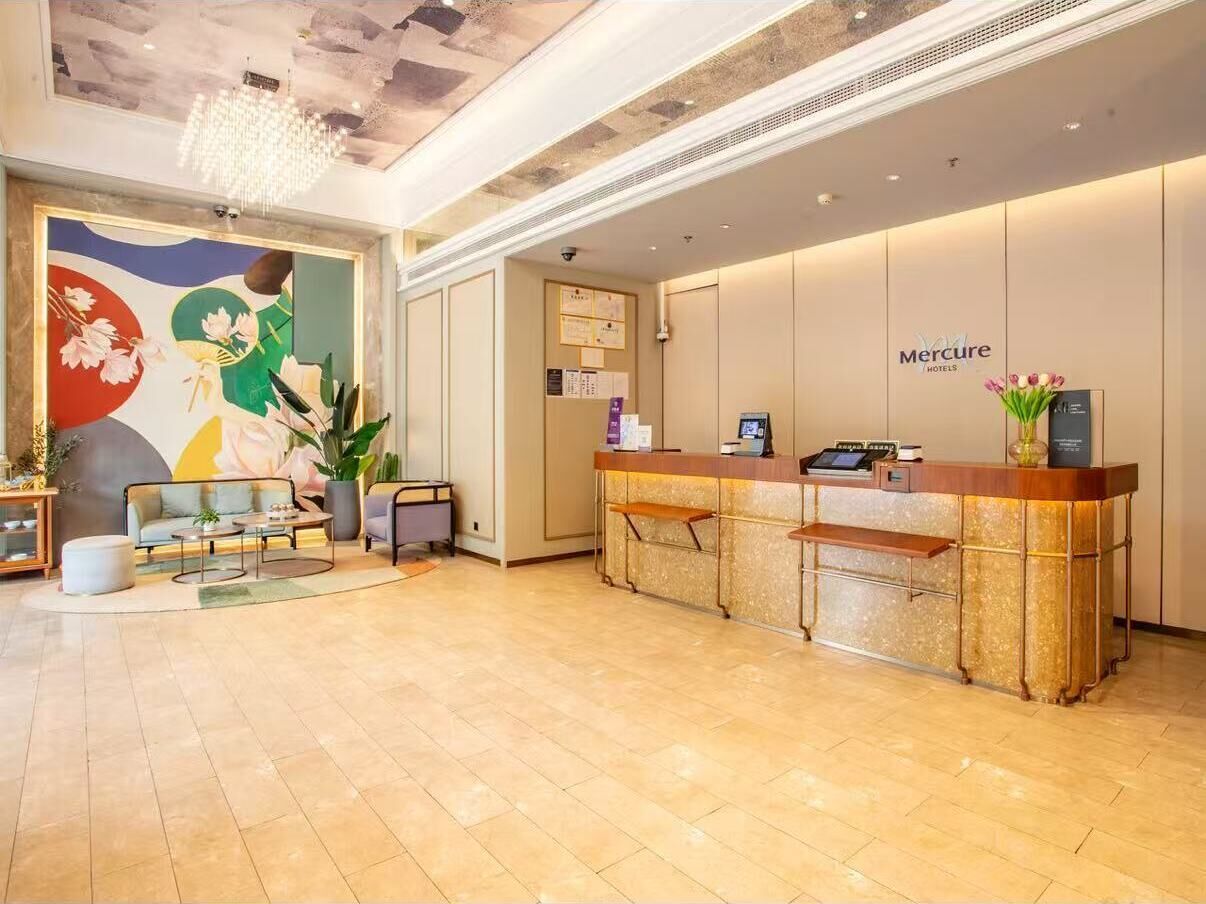 A hotel reception area with a reception desk, seating area, and a mural on the wall.