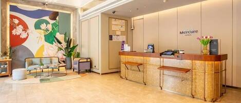 A hotel reception area with a reception desk, seating area, and a mural on the wall.